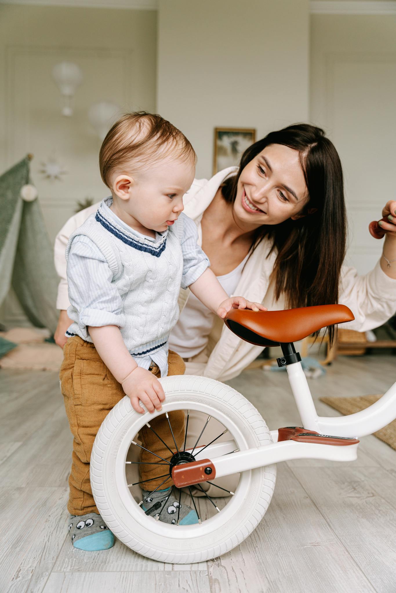 Mother and young child interact with a bicycle indoors, sharing joy and bonding.