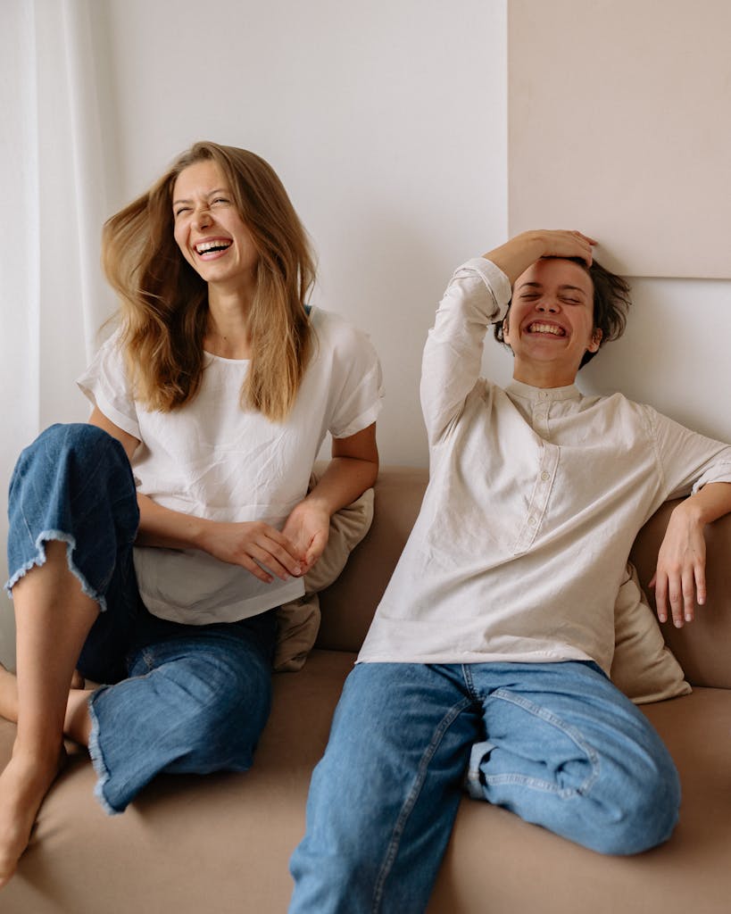 Two women enjoying a fun moment on a sofa, capturing genuine laughter and friendship.